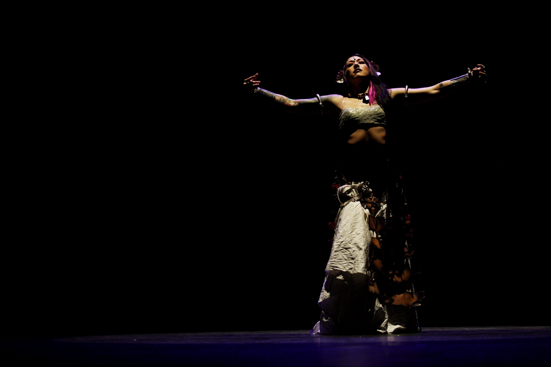 Sharon Kihara on a dark stage with her arms outstretched