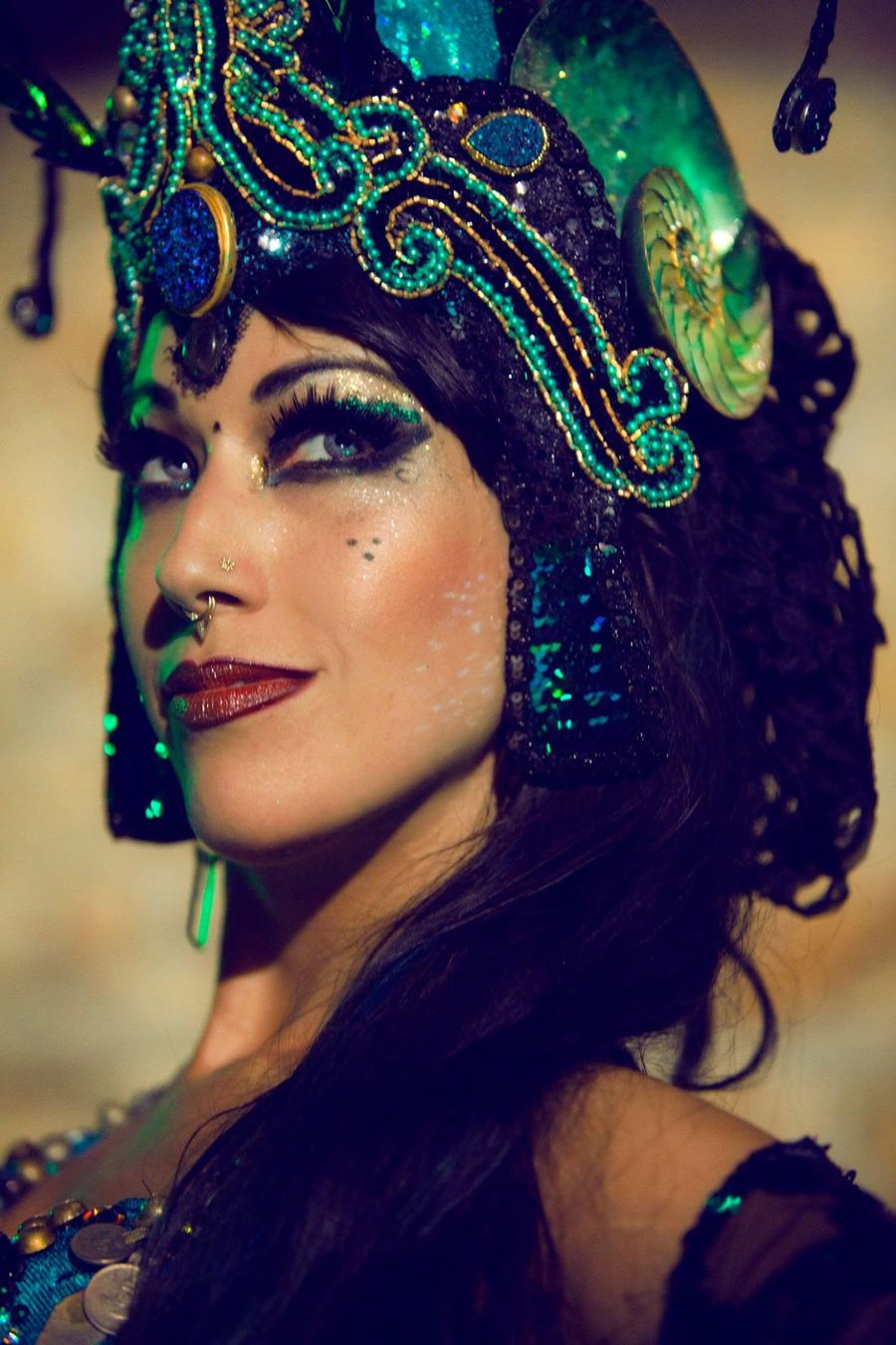 Portrait of Sharon Kihara in a teal and gold beaded headdress with a shell ornament, glittering eye makeup and dark red lips