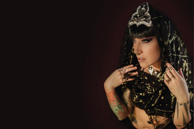 Press photo, landscape: close portrait of Sharon Kihara in a beaded black veil and a jeweled crown, hands raised to her chest
